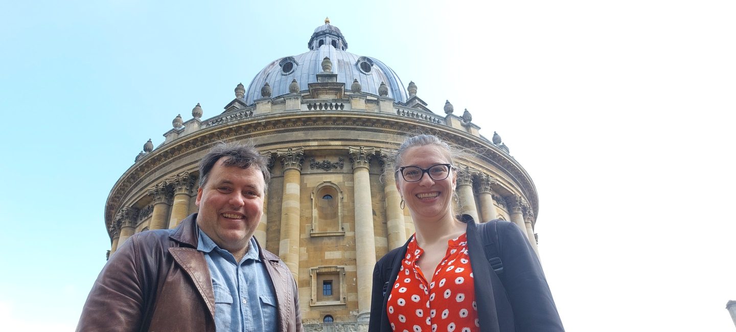 Aligned AI co-founders Stuart Armstrong and Rebecca Gorman standing in front of Oxford's Radcliffe Camera.