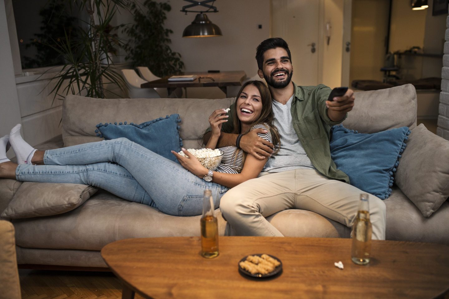 Young Couple Relaxing On Sofa, Chatting Smiling, eating popcorn and Changing Channels