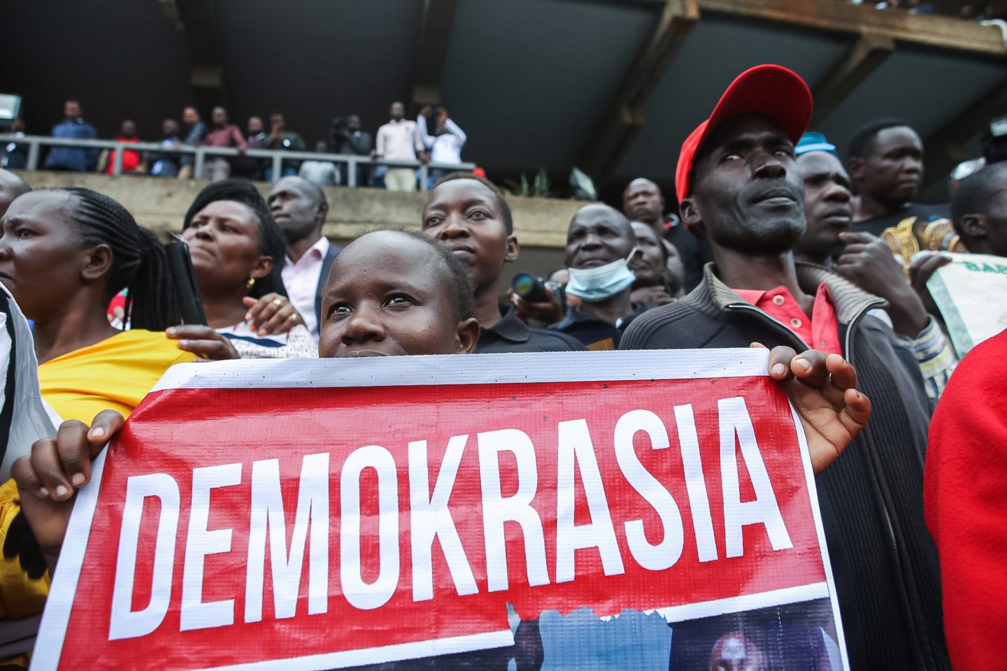 A Kenyan woman carrying a placard that says "Democracy" in "Swahili" listens to the Azimio la Umoja presidential candidate Raila Odinga at the Kenyatta International Convention Centre (KICC ) after the filing of the election petition challenging the presidential results of the just concluded general elections in Kenya held on 9 August 2022.