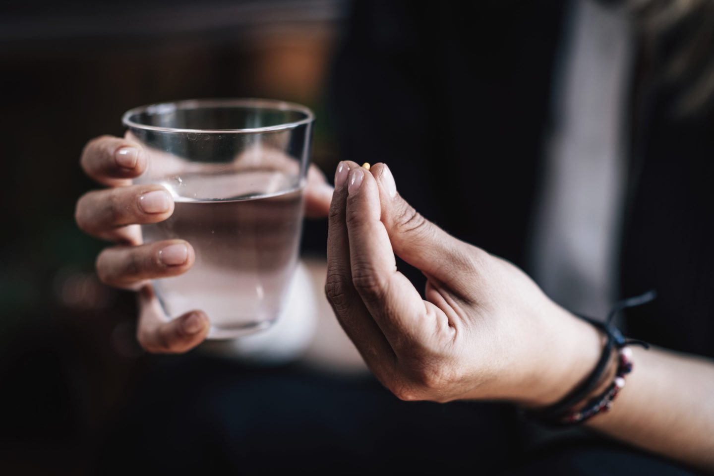 Close-up photo of hands holding a pill and a cup of water