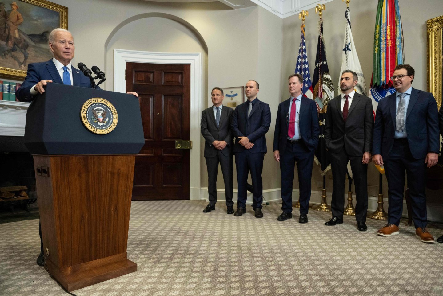 President Biden speaks at a podium in the White House while representatives from seven leading A.I. companies stand by watching.