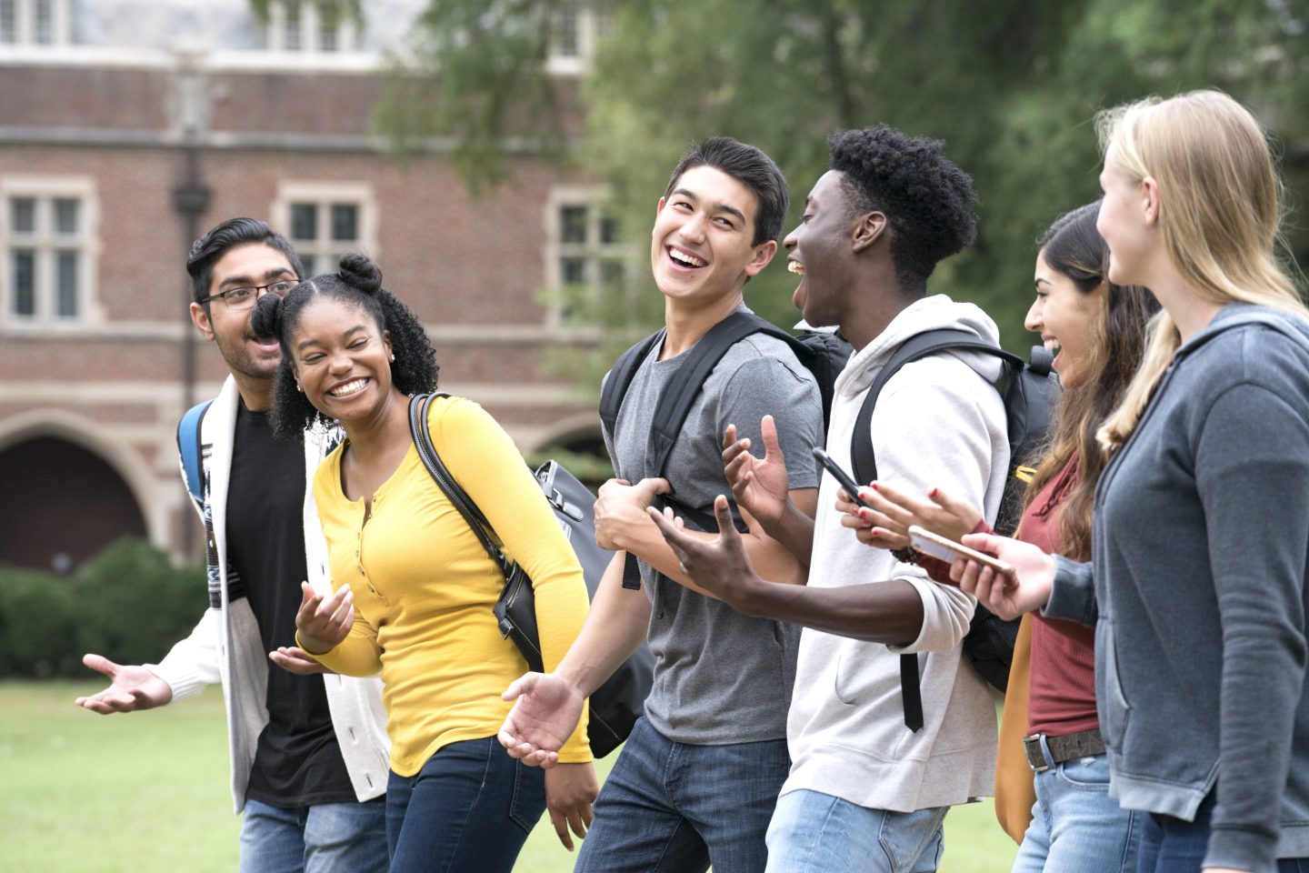 A group of college students laugh as they walk through campus.